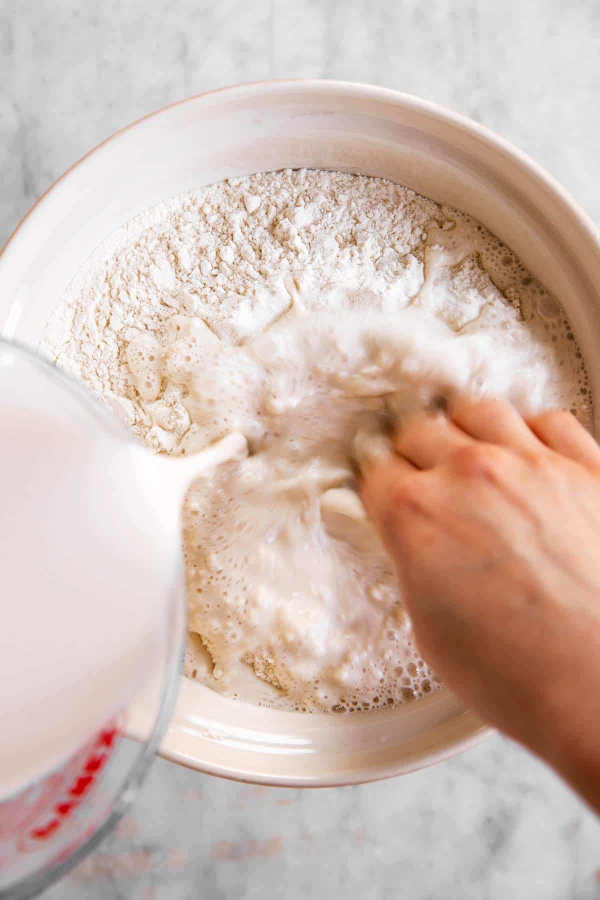 female hands stirring dissolved sourdough starter into bowl with flour