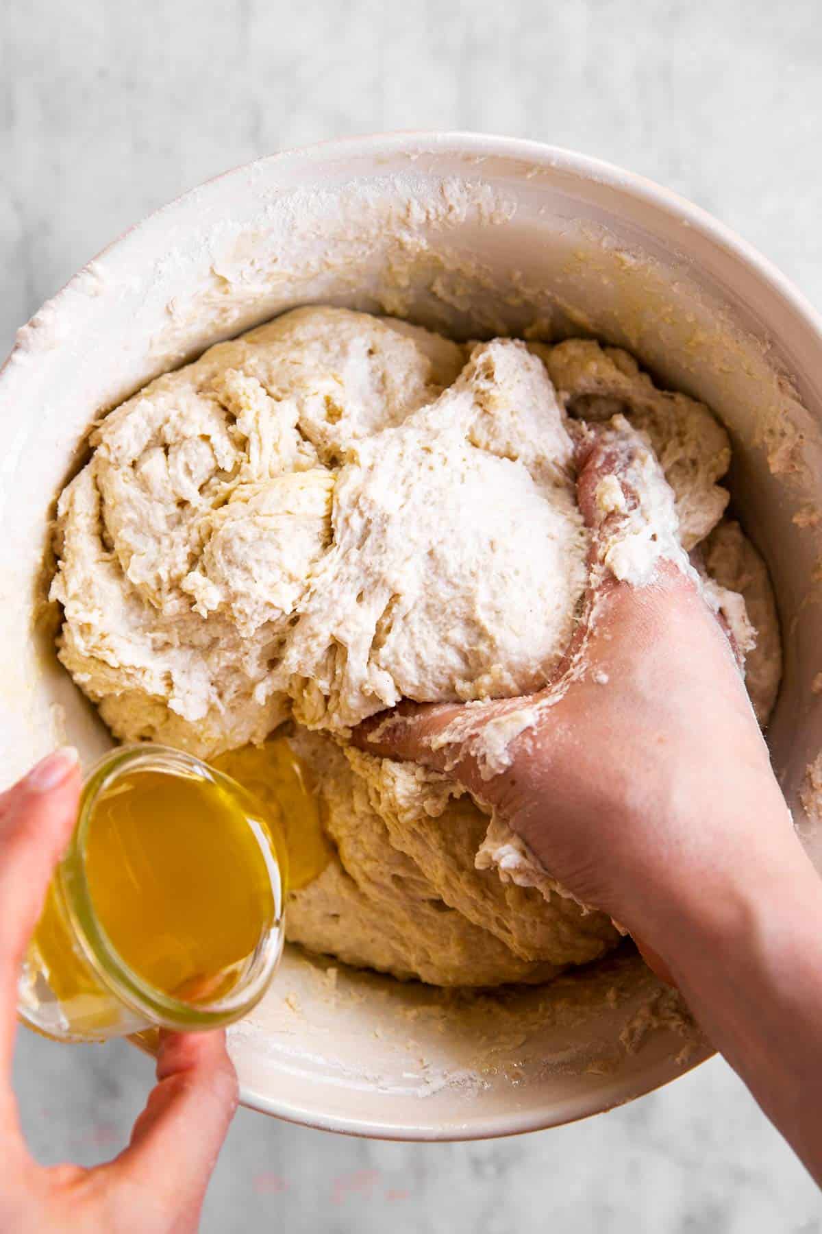 female hands pouring olive oil over sourdough bread dough in bowl