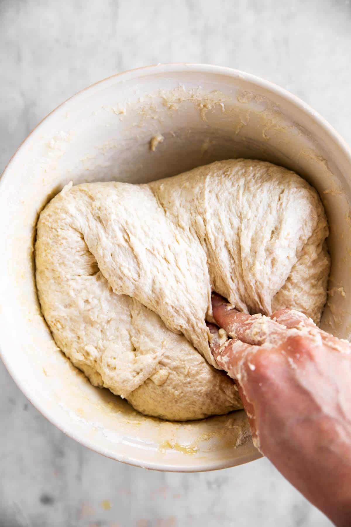 female hand folding sourdough bread dough in white mixing bowl