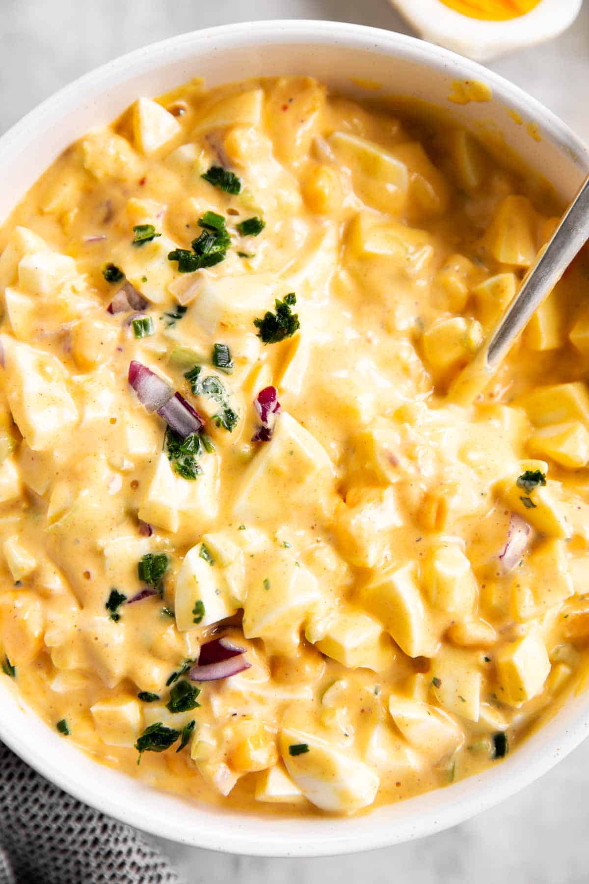 overhead close up view of egg salad topped with chives and red onion in white bowl