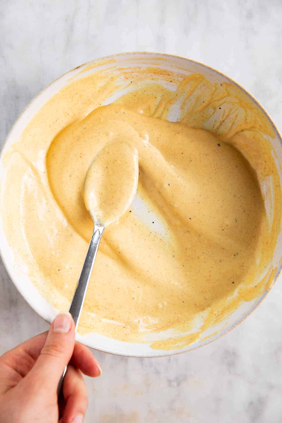 female hand using spoon to stir sauce for egg salad in white bowl