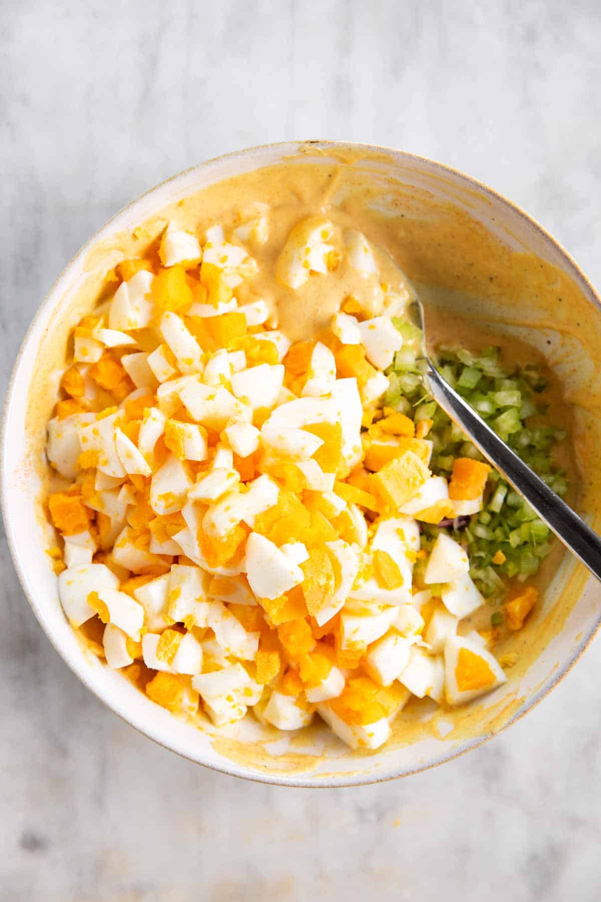 ingredients for a classic egg salad in white bowl with a spoon