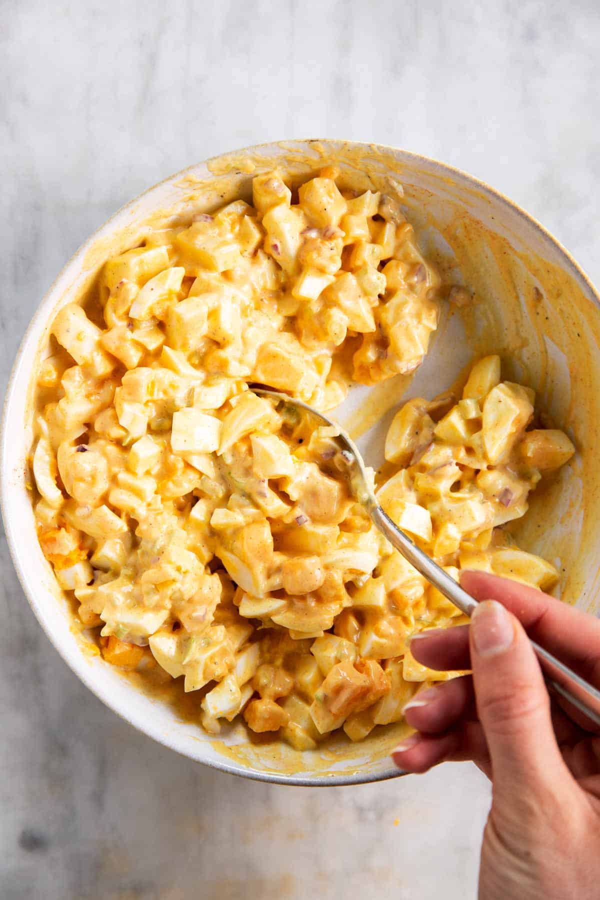 female hand stirring egg salad in white bowl