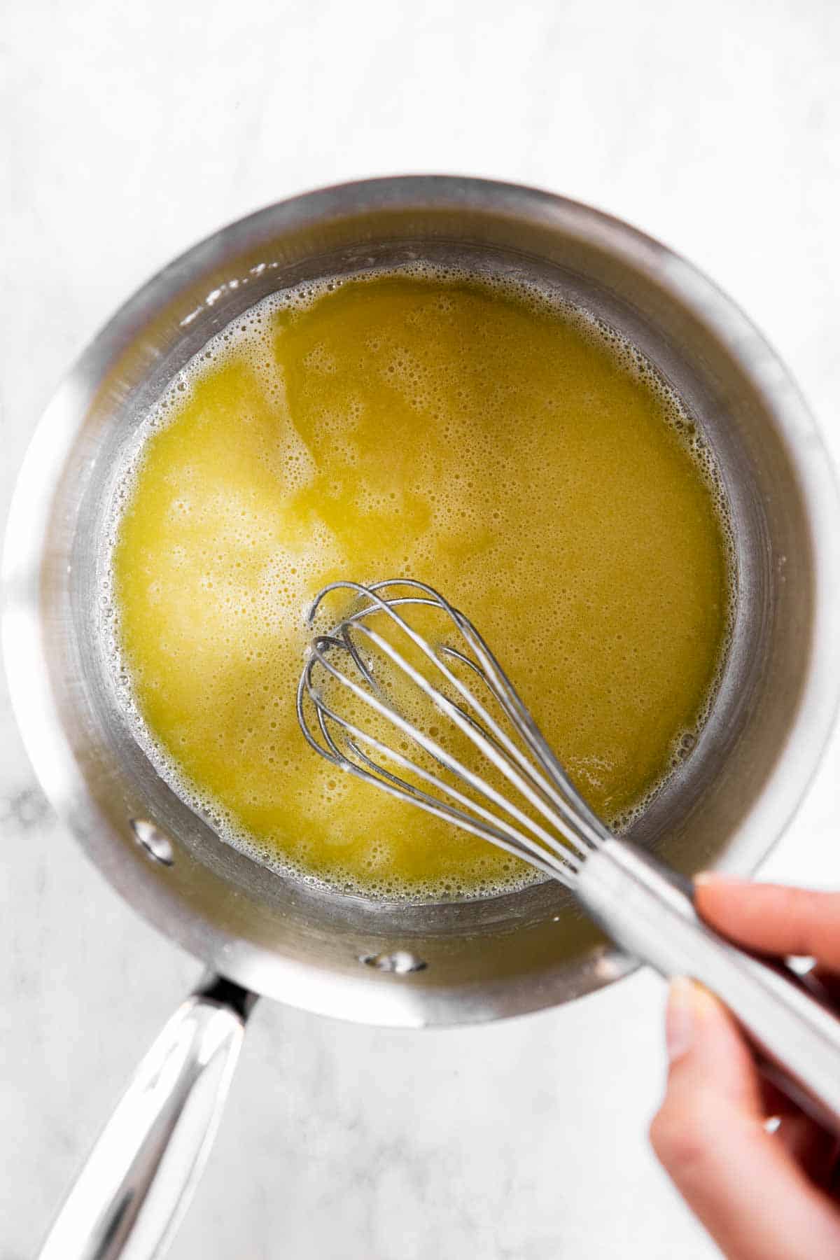 female hand whisking flour in olive oil in small saucepan