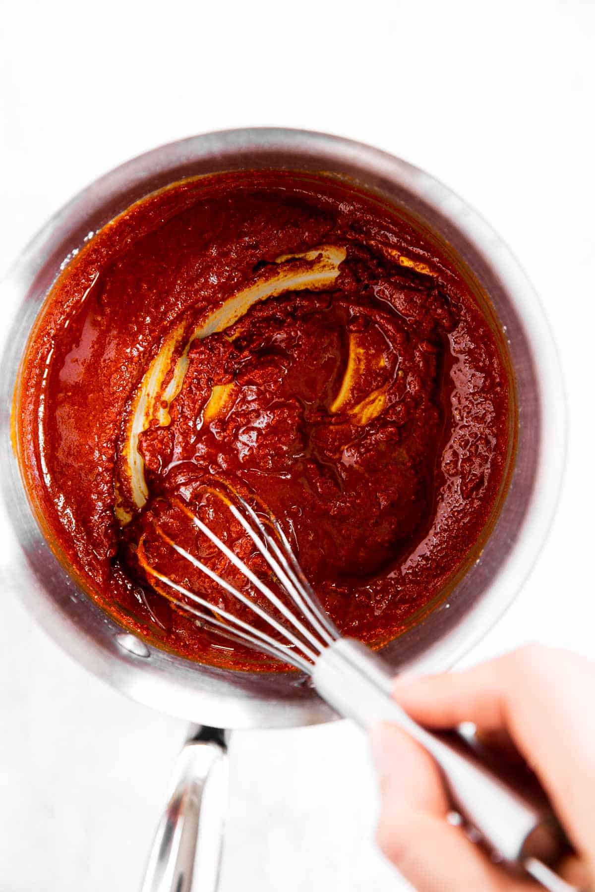 female hand whisking tomato paste in small saucepan