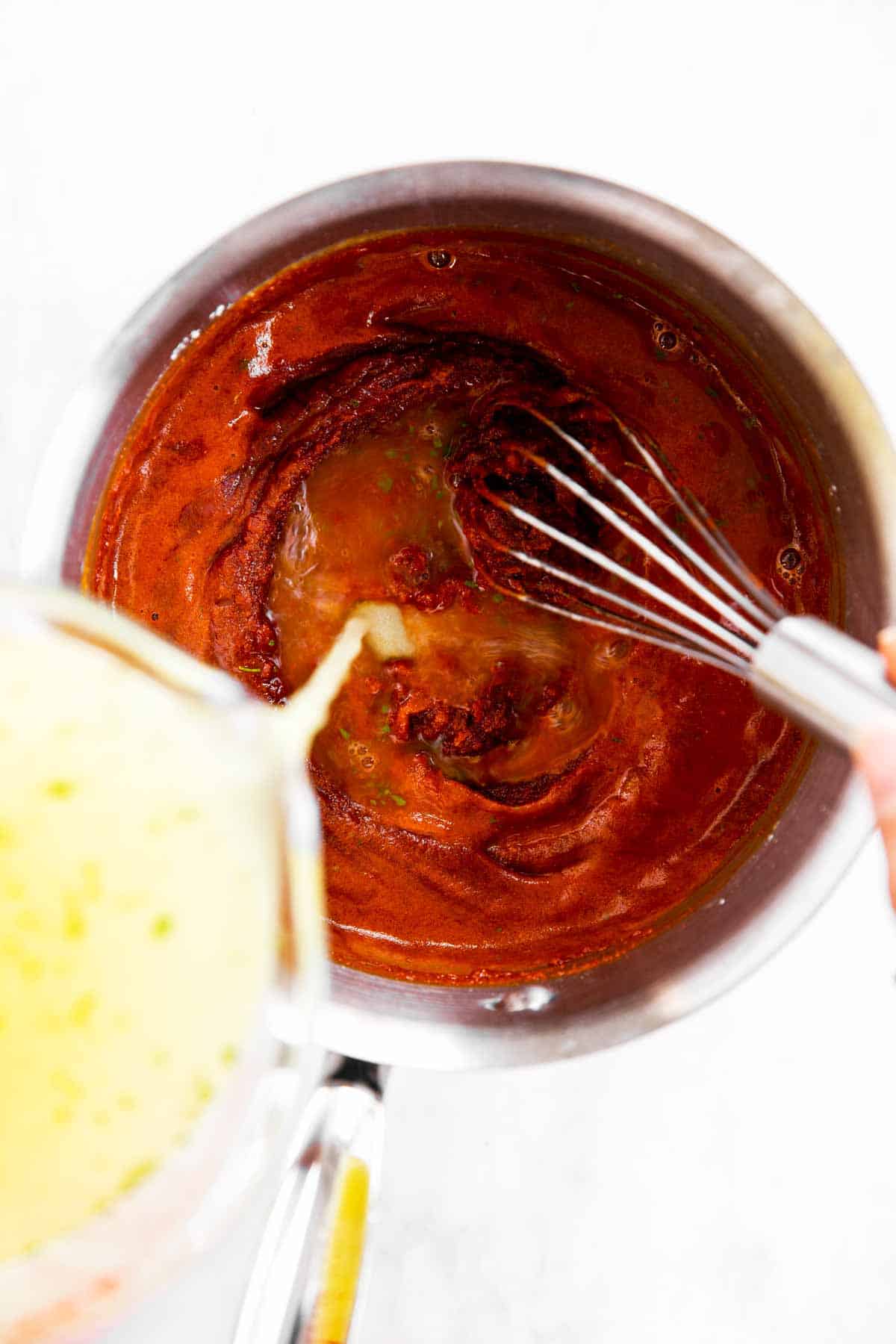 female hand whisking chicken broth into tomato roux in small saucepan