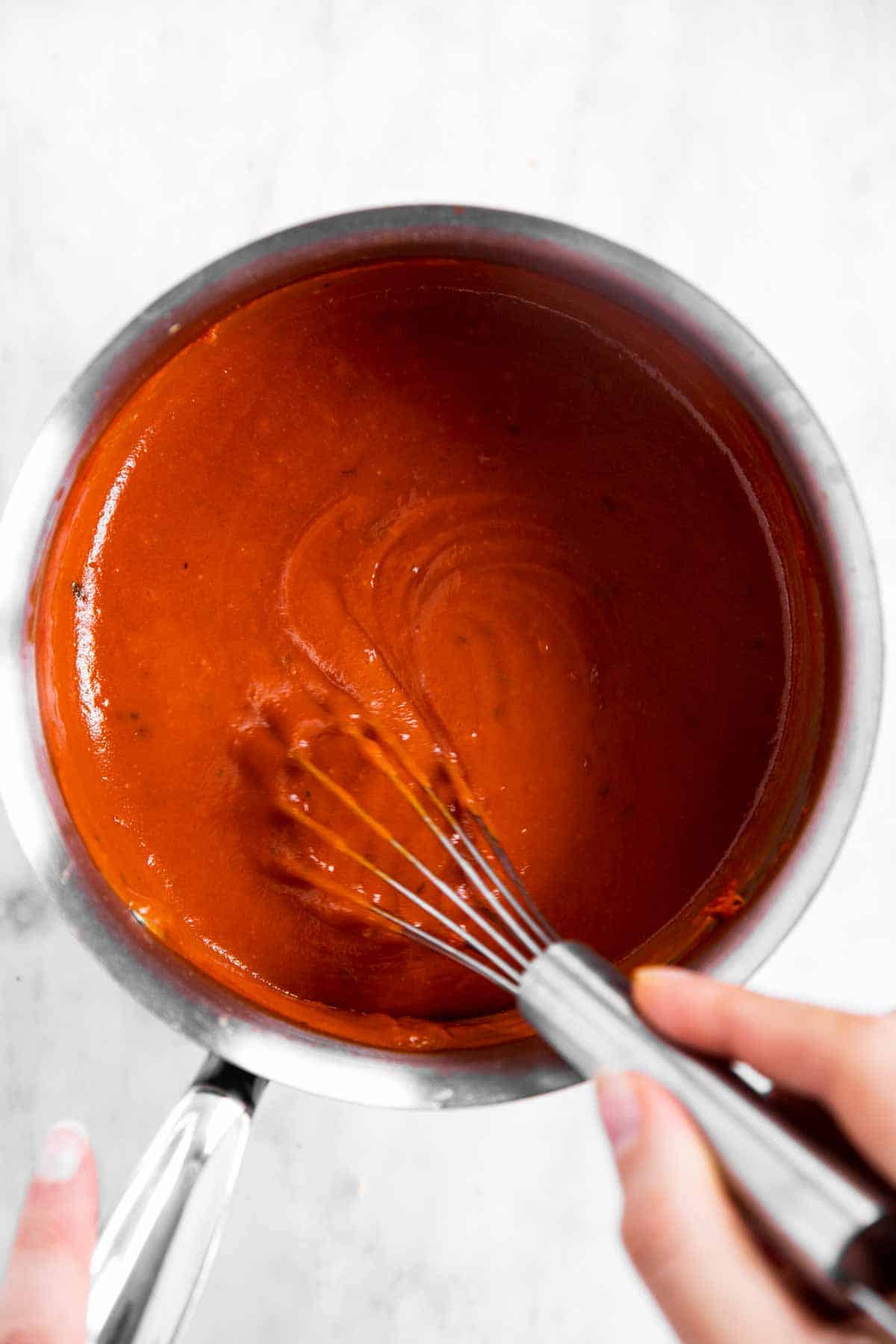 female hand whisking cooked enchilada sauce