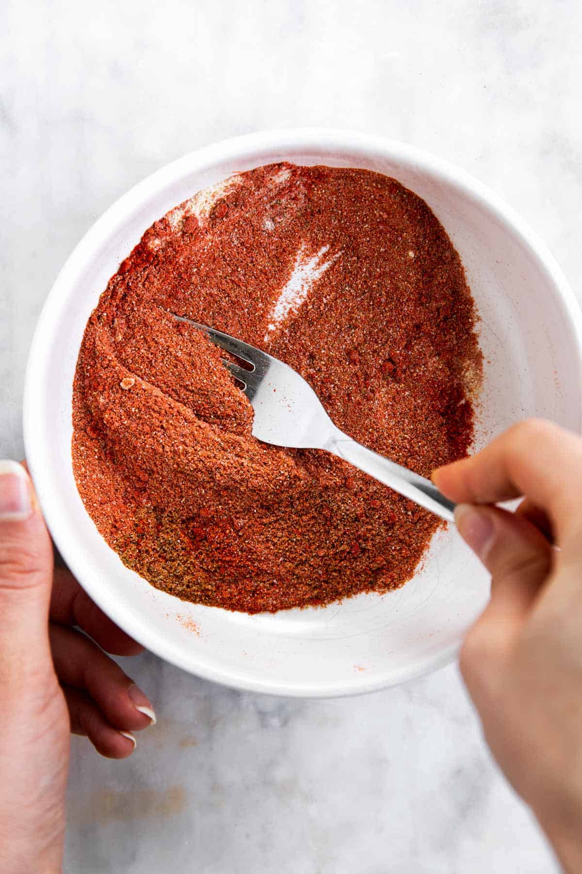 female hands mixing fajita spices with a fork in a white bowl