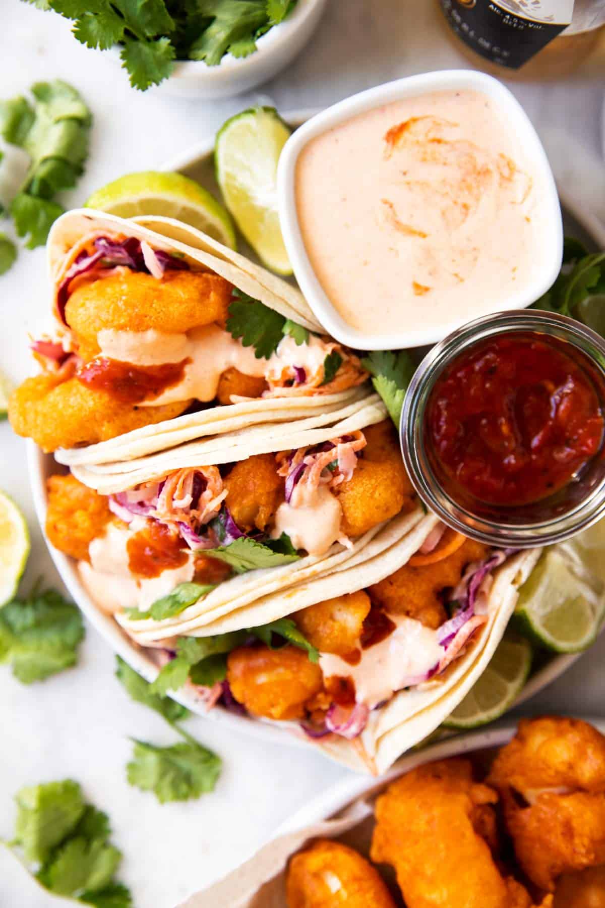 overhead view of fish tacos on plate with sauces surrounded by fresh cilantro