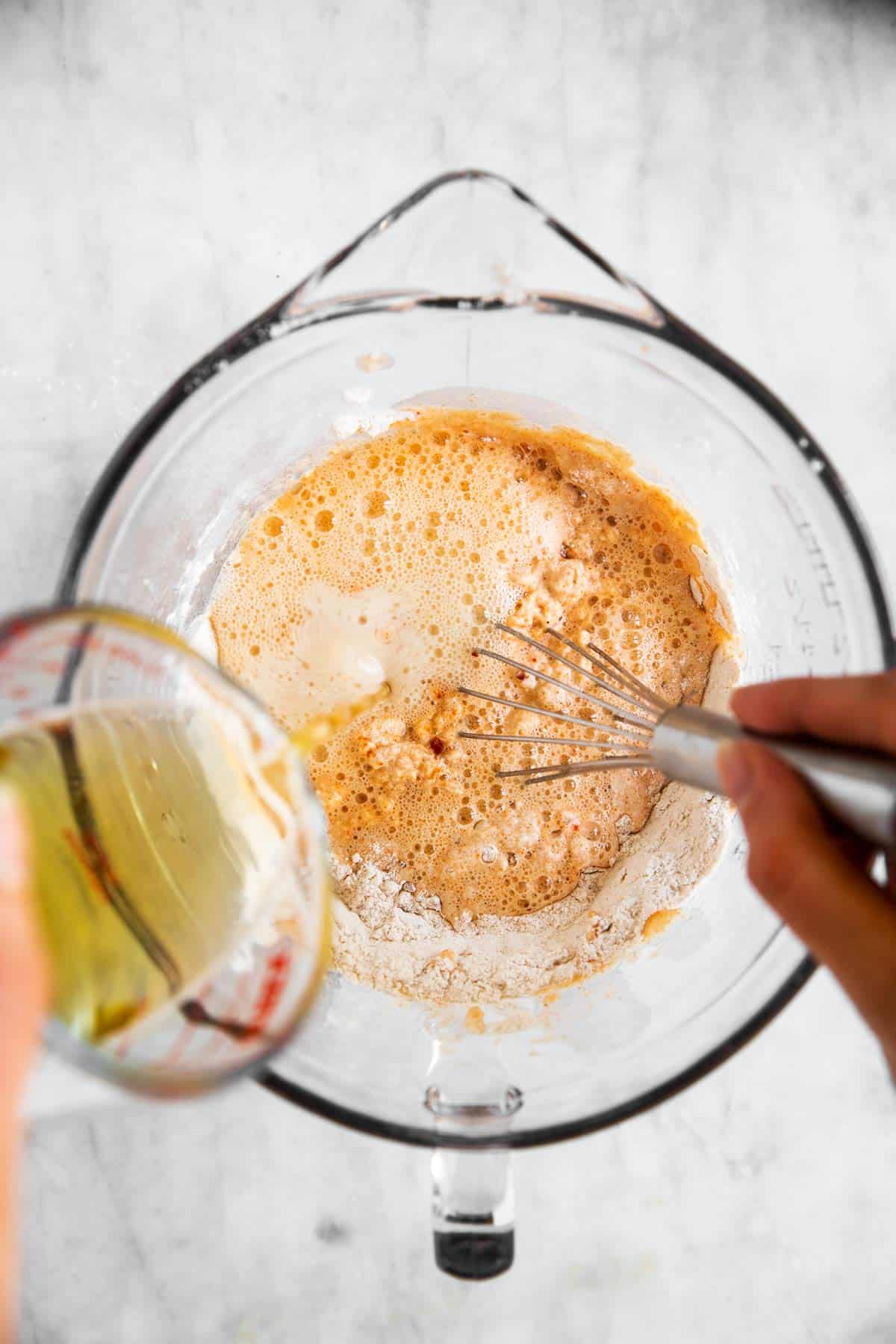 female hand whisking beer into batter in glass bowl