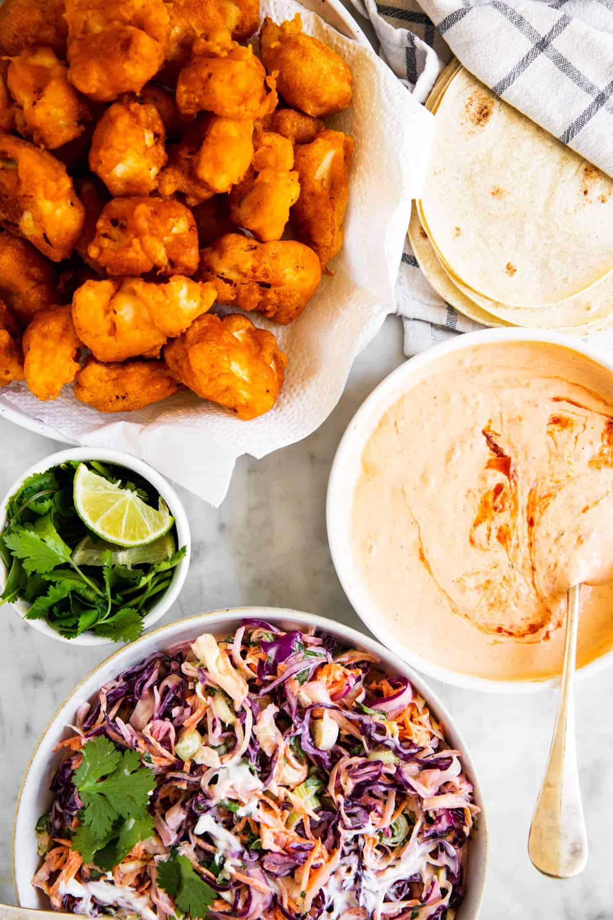 battered fried fish, taco shells, slaw, chipotle mayo, cilantro and lime on marble surface