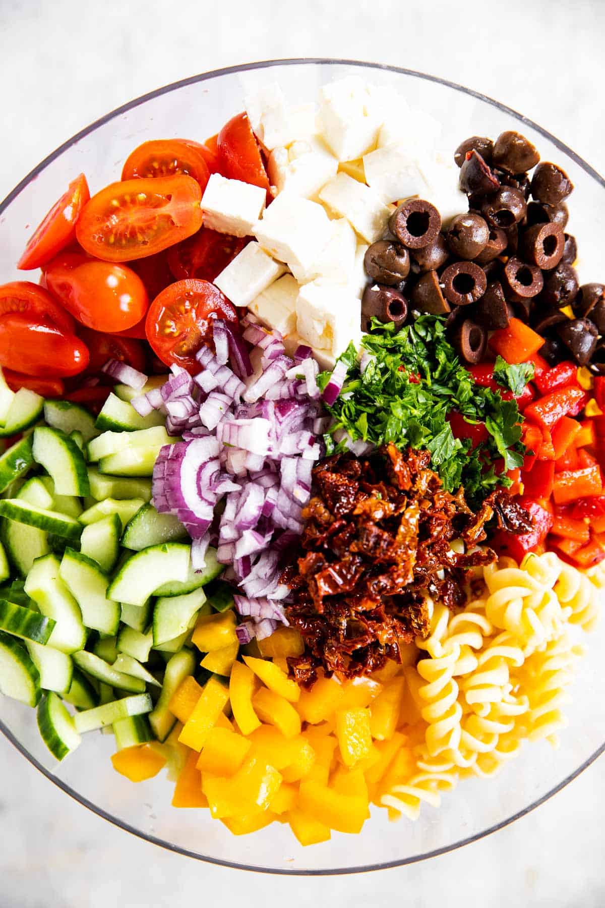 ingredients for greek pasta salad in glass bowl