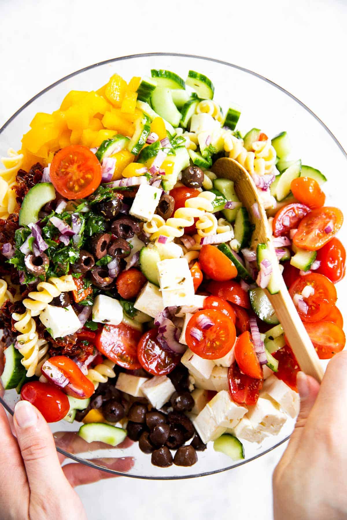 female hands stirring greek pasta salad