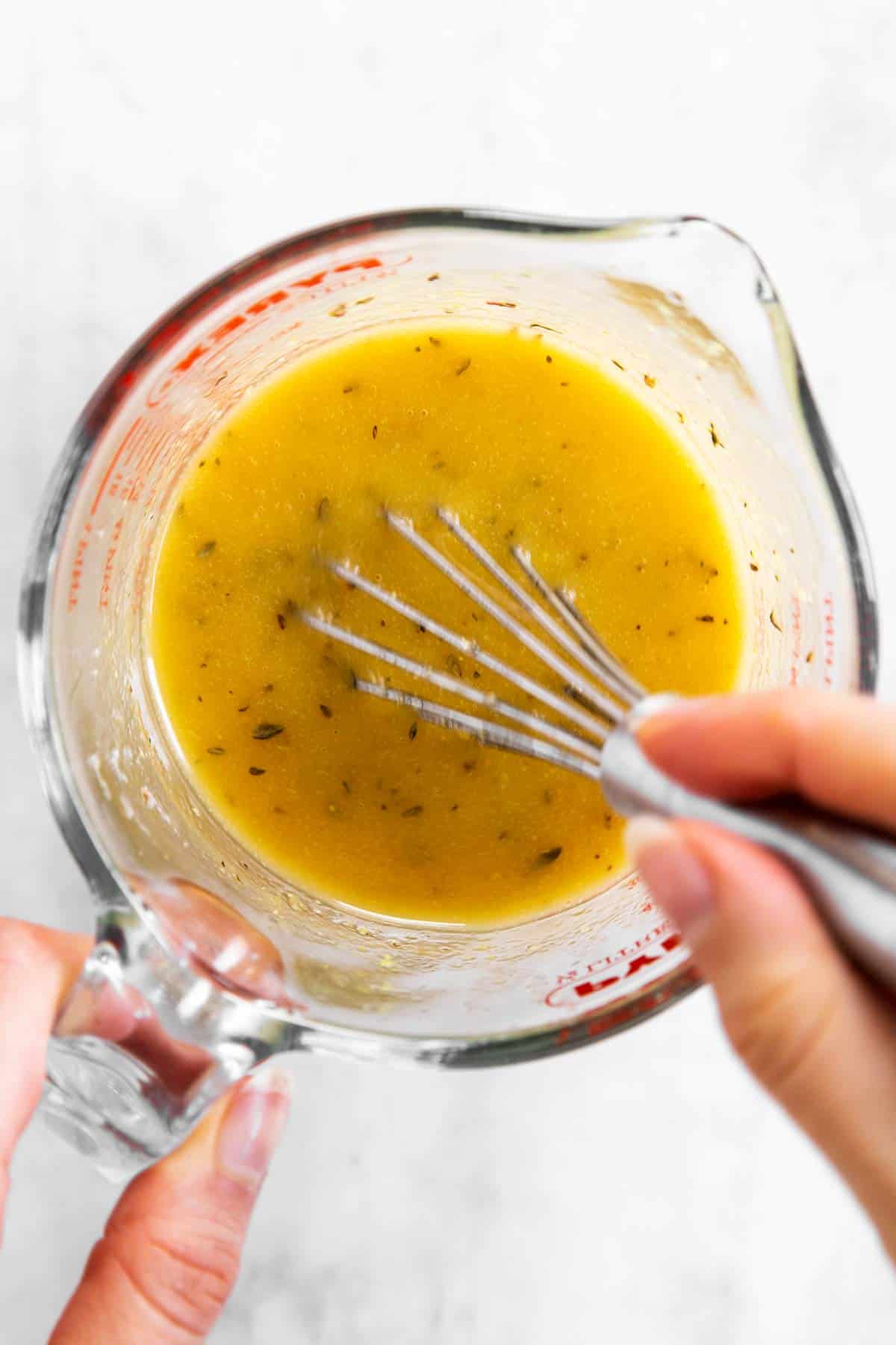 female hand mixing Greek salad dressing in glass measuring jug with a whisk