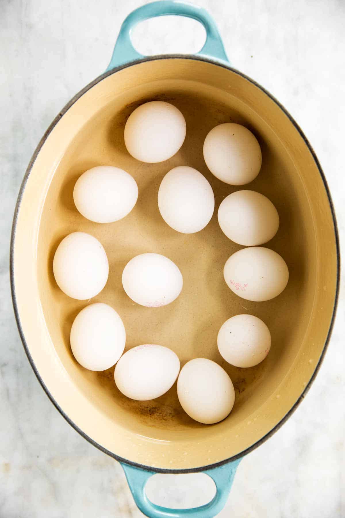 raw eggs in shell covered in water in oval Dutch oven