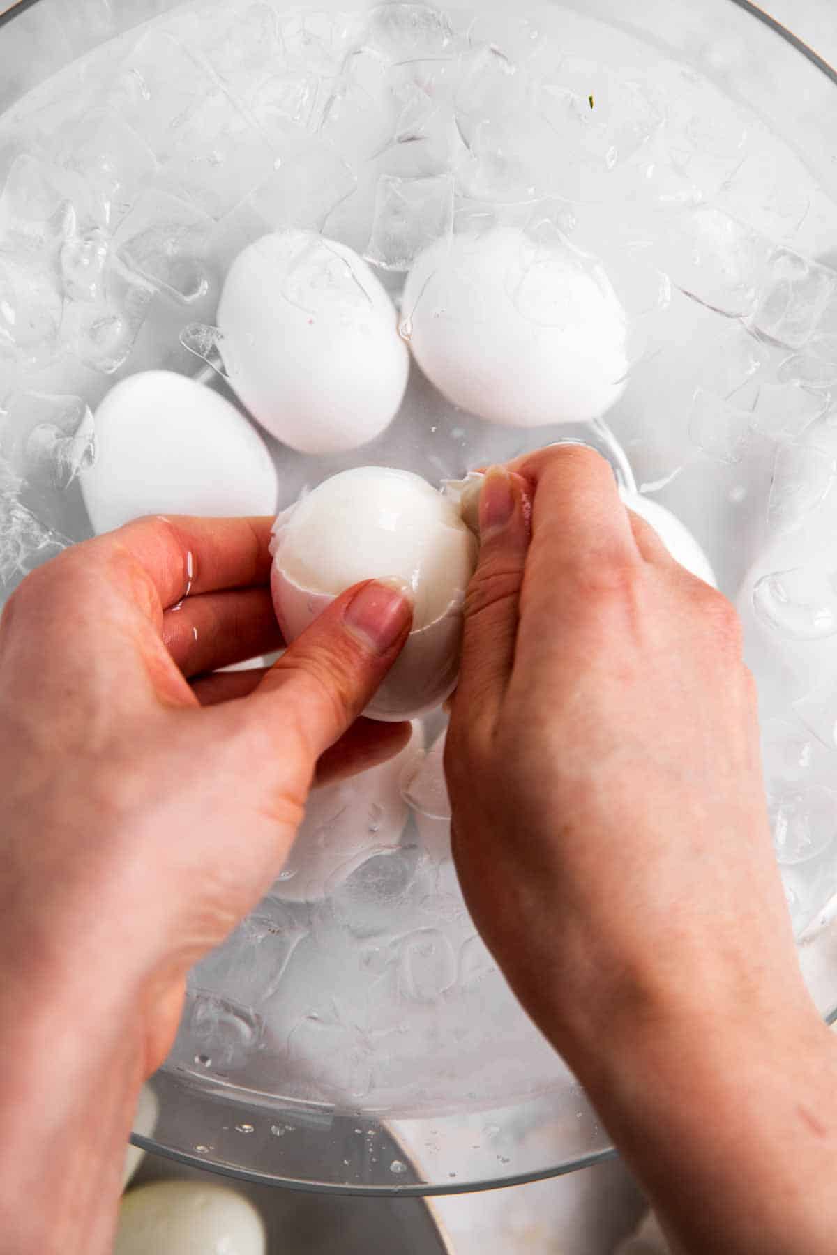 female hand peeling hard boiled egg in bowl with water