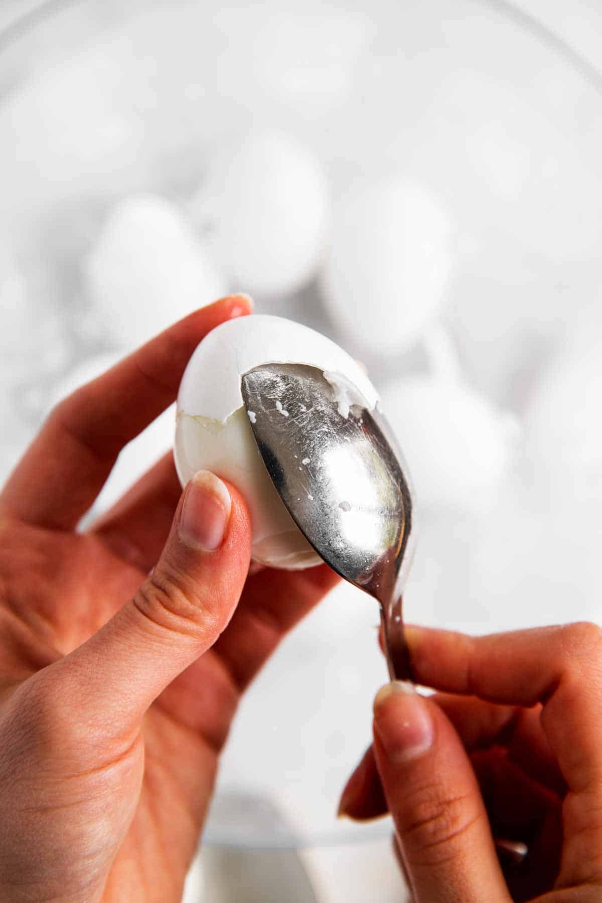 female hand releasing egg shell from hard boiled egg with help of a tablespoon