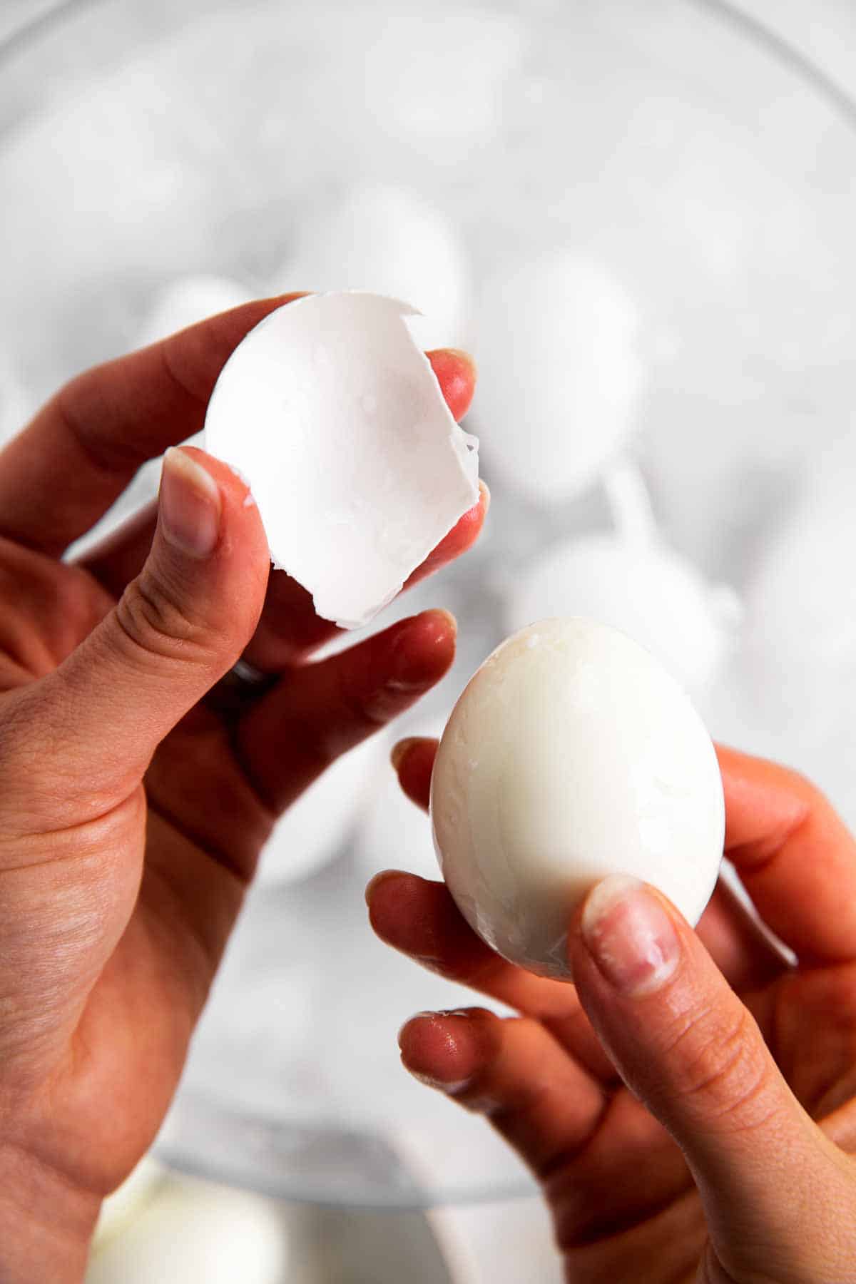 left hand holding egg shell with right hand holding peeled hard boiled egg