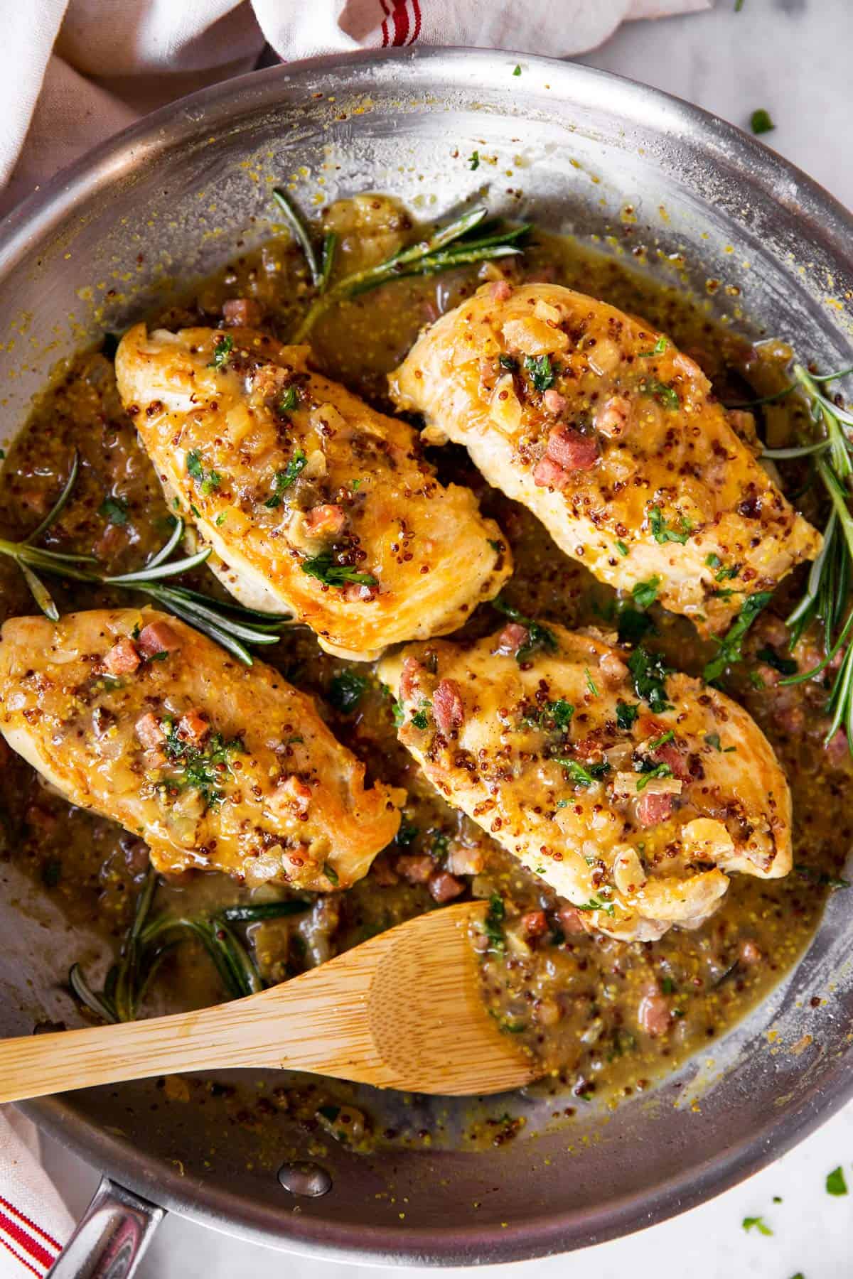 overhead view of four chicken breasts in skillet with honey mustard sauce, bacon and fresh rosemary