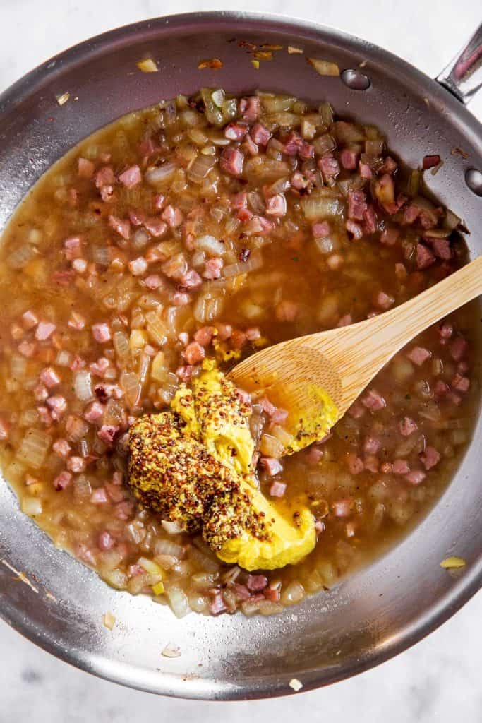 deglazed pan with onion and bacon, with two types of mustard spooned into sauce