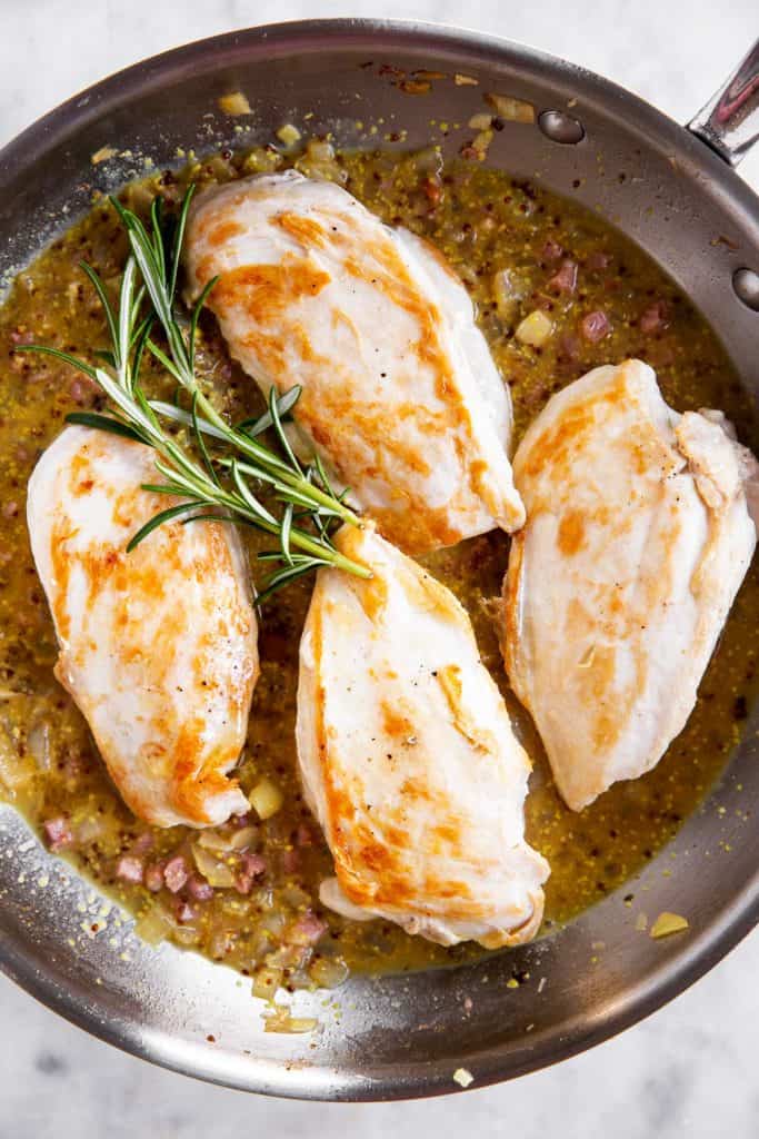 uncooked, seared chicken on top of honey mustard sauce in skillet with fresh rosemary