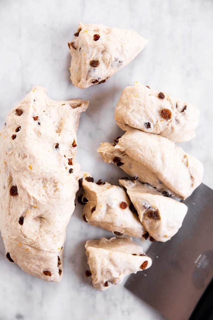 hot cross bun dough divided into 6 smaller and 1 large piece with a dough scraper