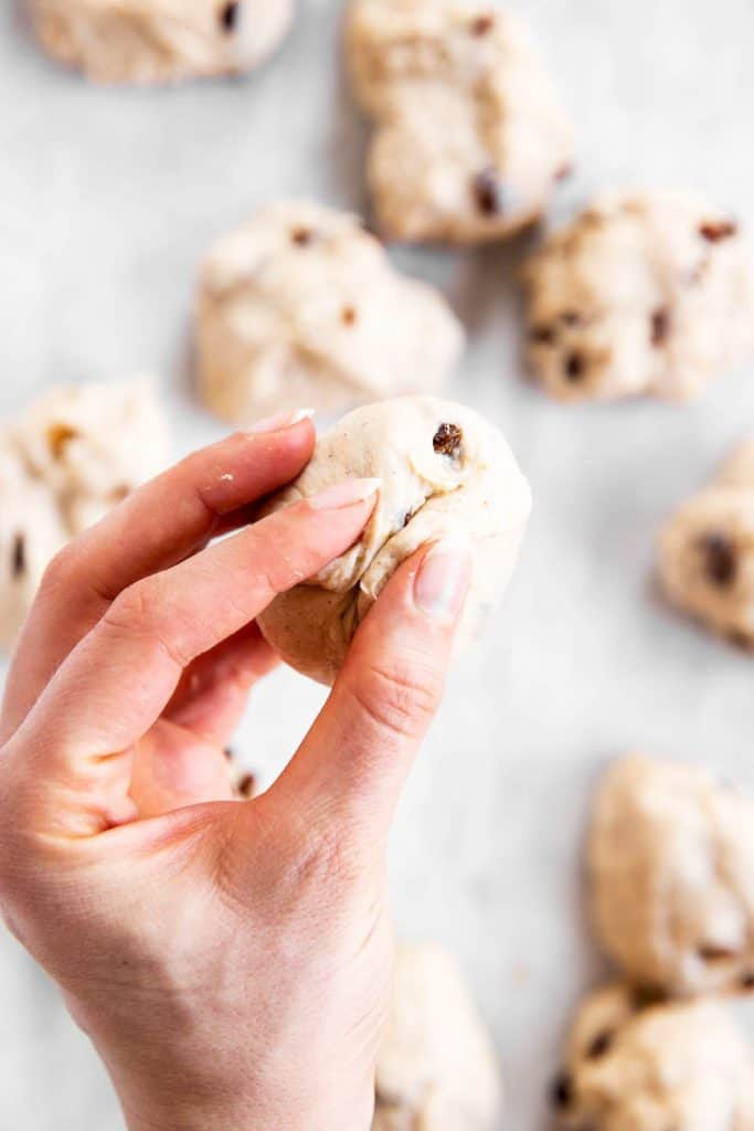 female hand pinching seams on bottom of unbaked hot cross bun roll