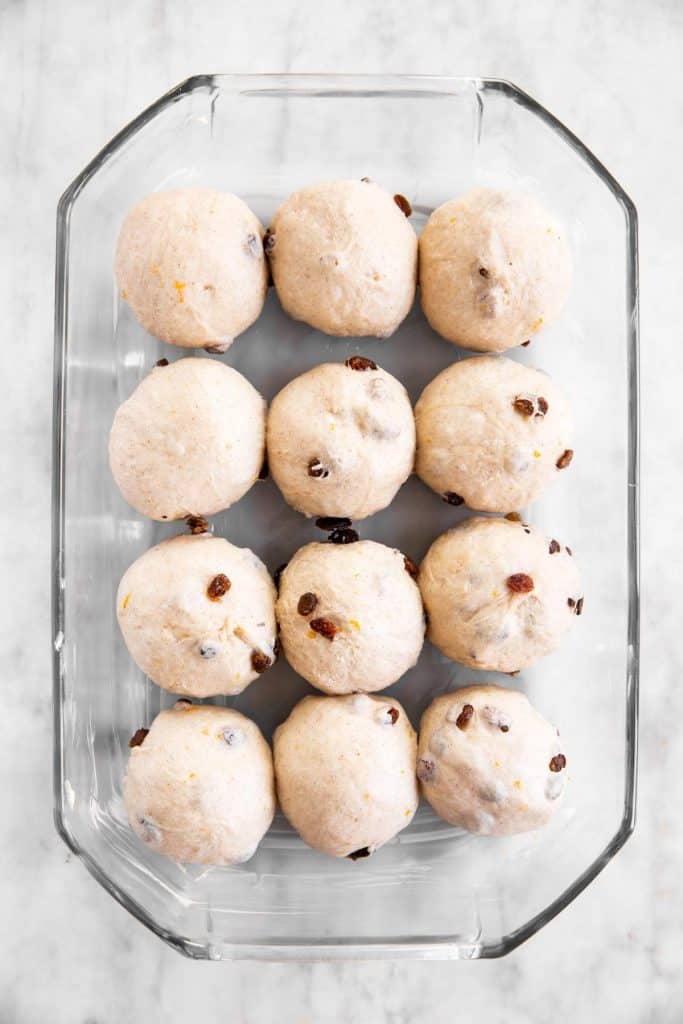 unbaked hot cross buns in glass pan before third rise