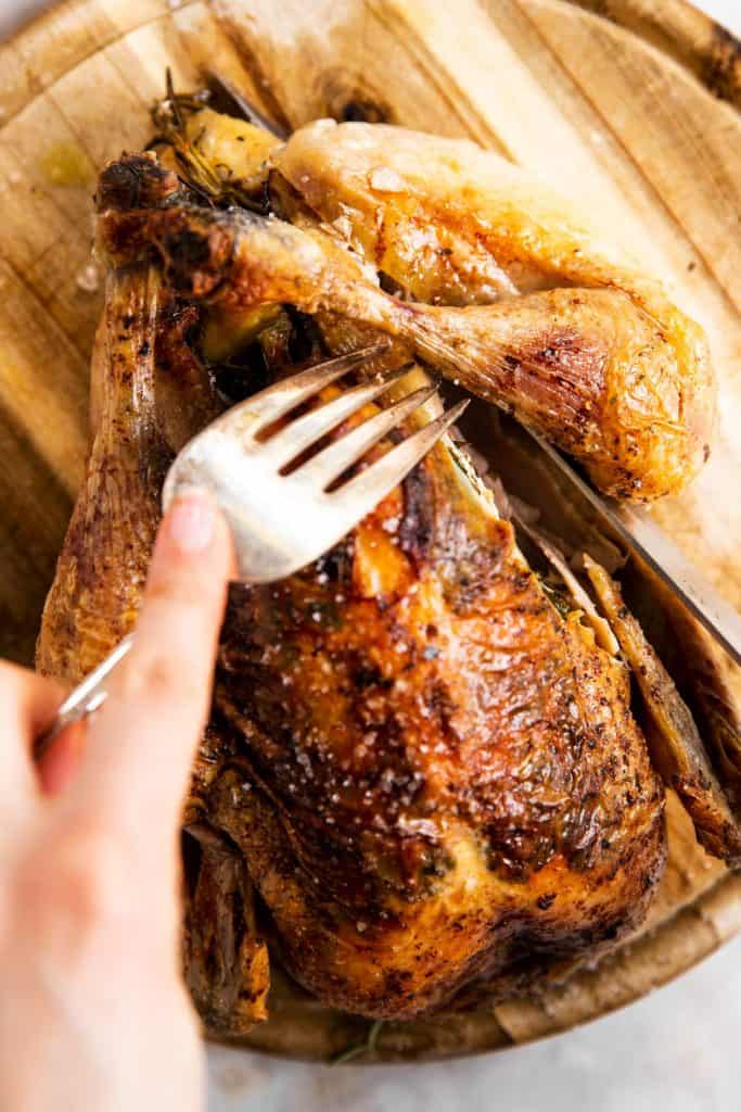 slicing a leg off a whole roasted chicken with a large fork and a carving knife