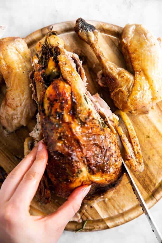 slicing a wing off a whole roasted chicken with a large fork and a carving knife
