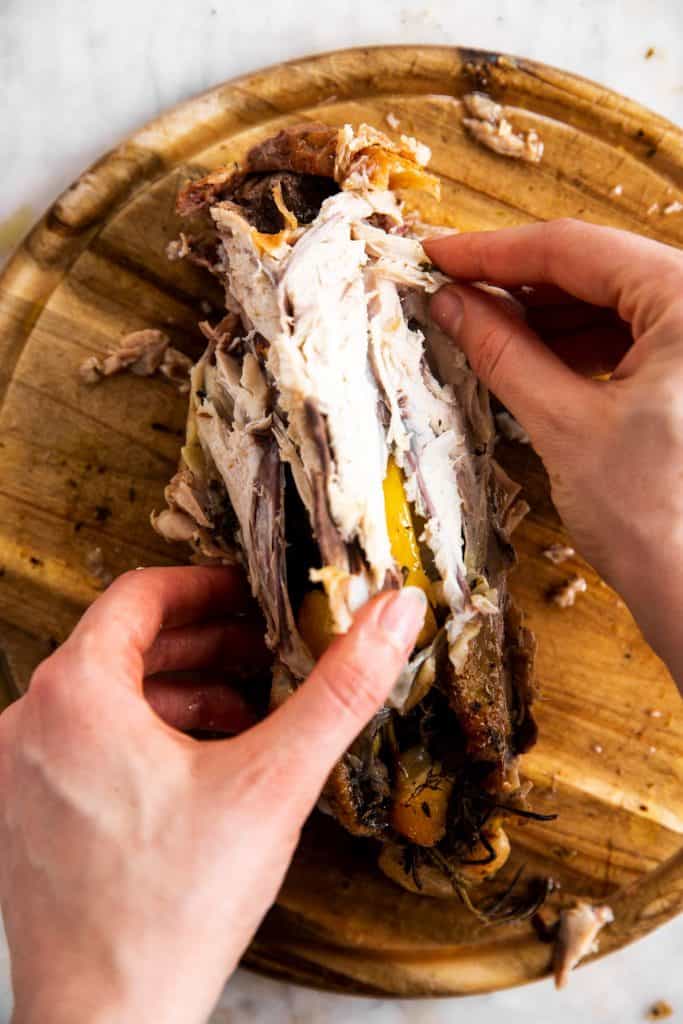 female hands picking meat off the carcass of a whole roasted chicken