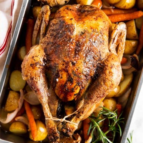 overhead view of whole roasted chicken in roasting pan with carrots and potatoes
