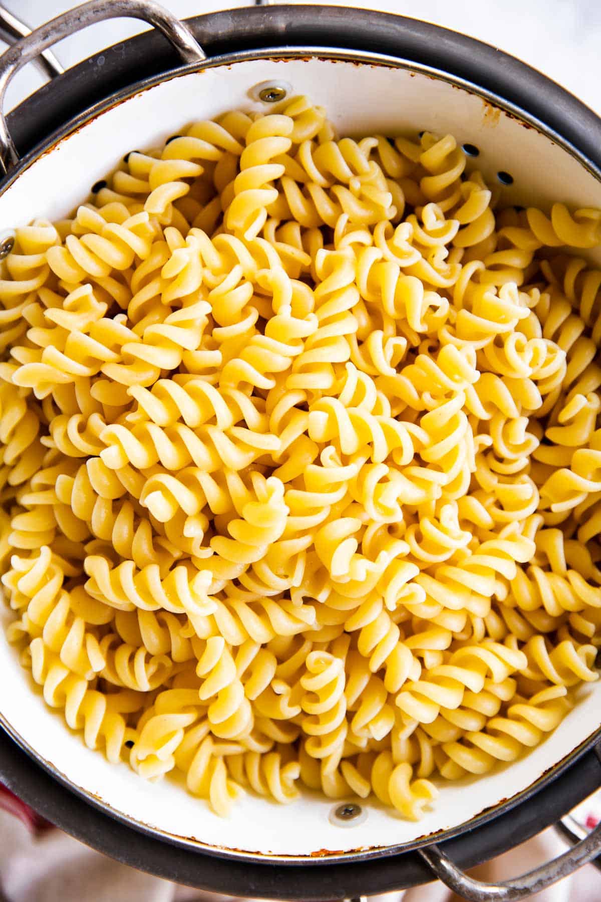 overhead view of cooked spiral pasta in white colander set over large pot