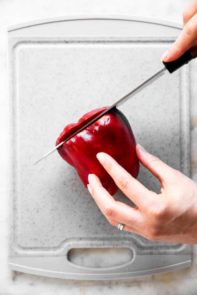 female hand slicing top off a red bell pepper