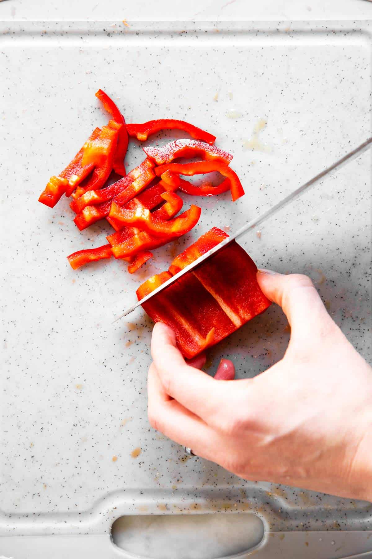 female hand slicing red bell pepper into thin slices