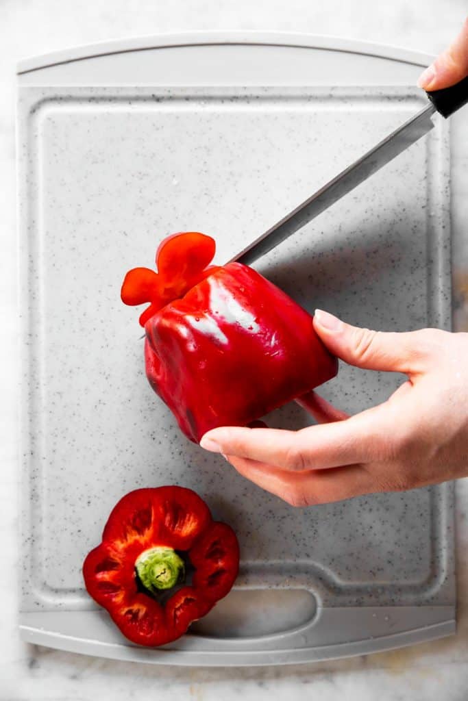 female hand slicing bottom off a red bell pepper