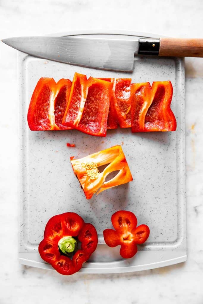 sliced bell pepper and core on grey chopping board with a chef's knife