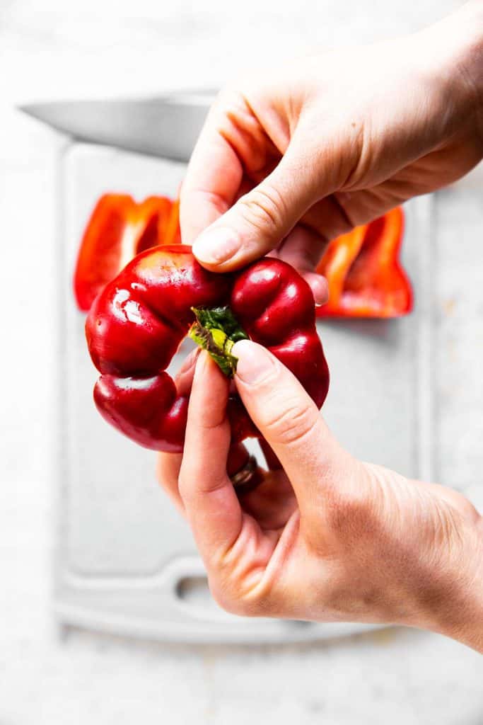 female hand removing green stem from bell pepper top