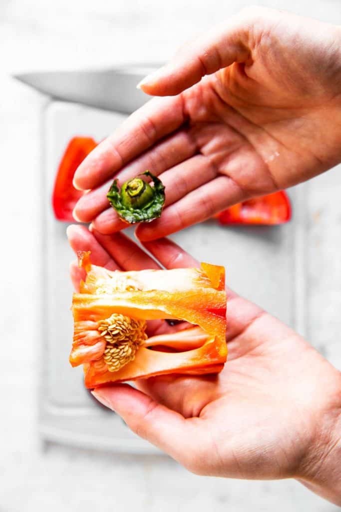 female hands holding core and stem from a red bell pepper