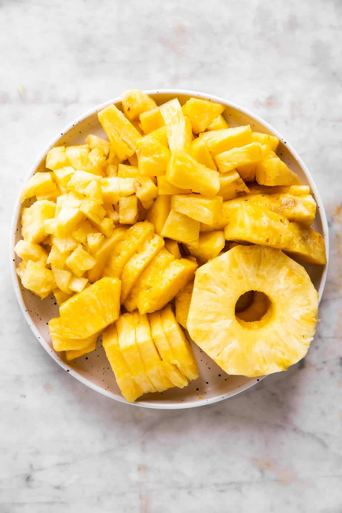 white plate filled with cut up pineapple in different shapes