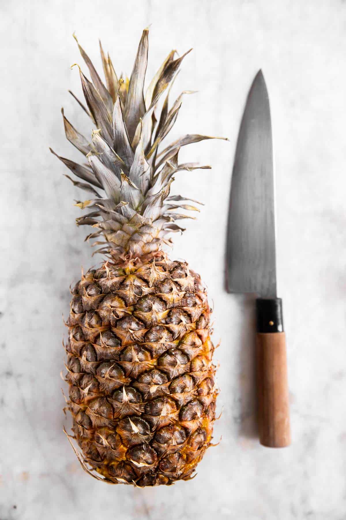 whole pineapple and chef's knife on white marble surface