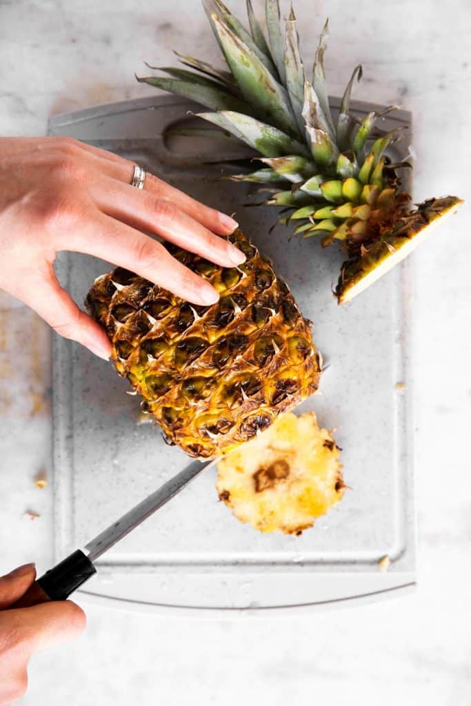 female hand trimming bottom off a pineapple