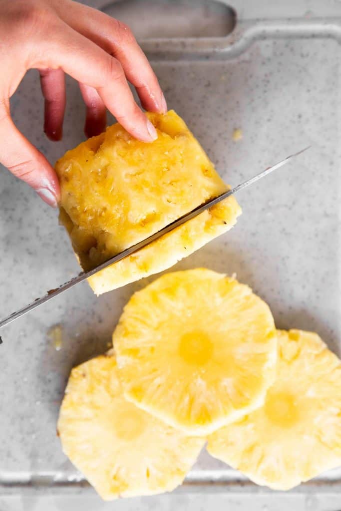 female hand cutting pineapple into rounds