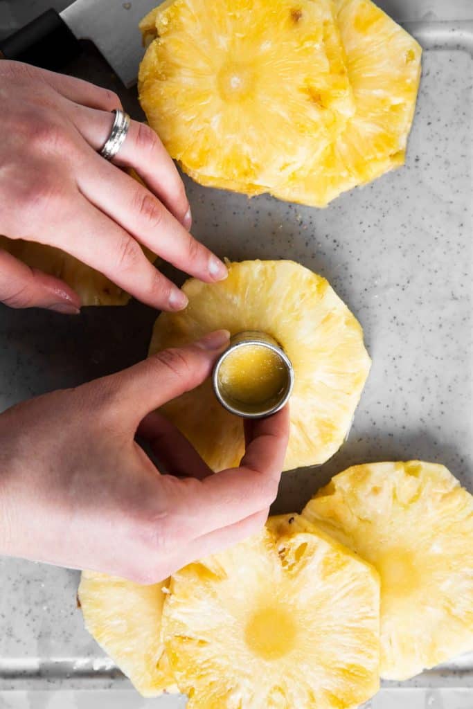 female hand using cookie cutter to remove core from pineapple slice