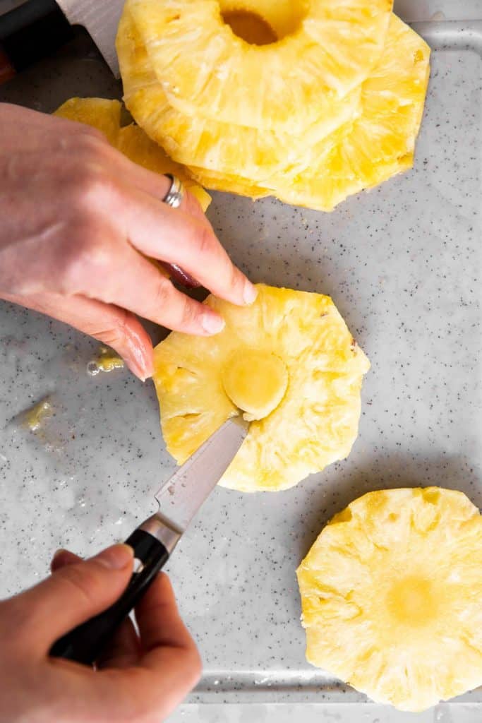 female hand using paring knife to remove core from pineapple slice