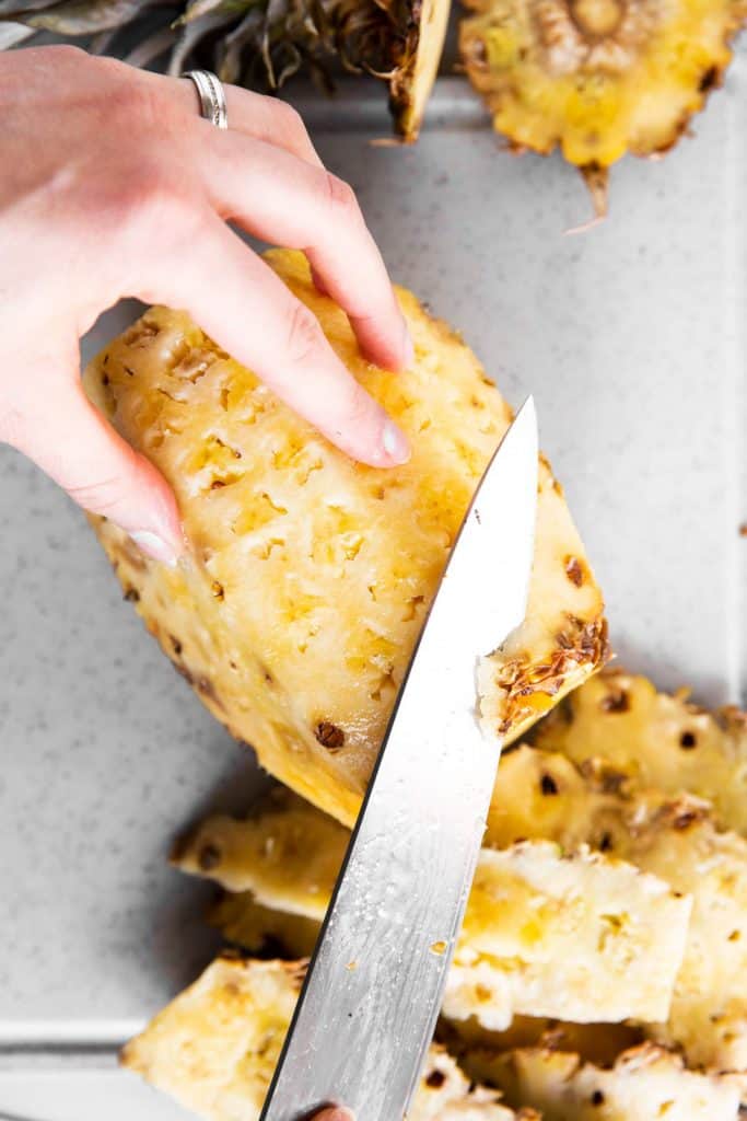 female hand slicing leftover skin off a pineapple