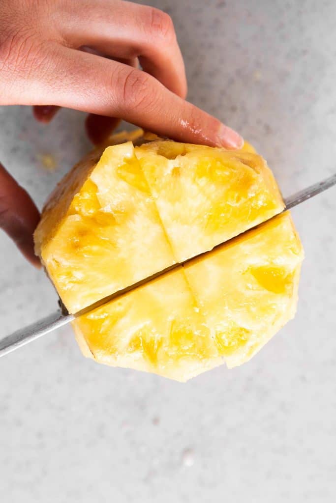 female hands quartering a peeled pineapple