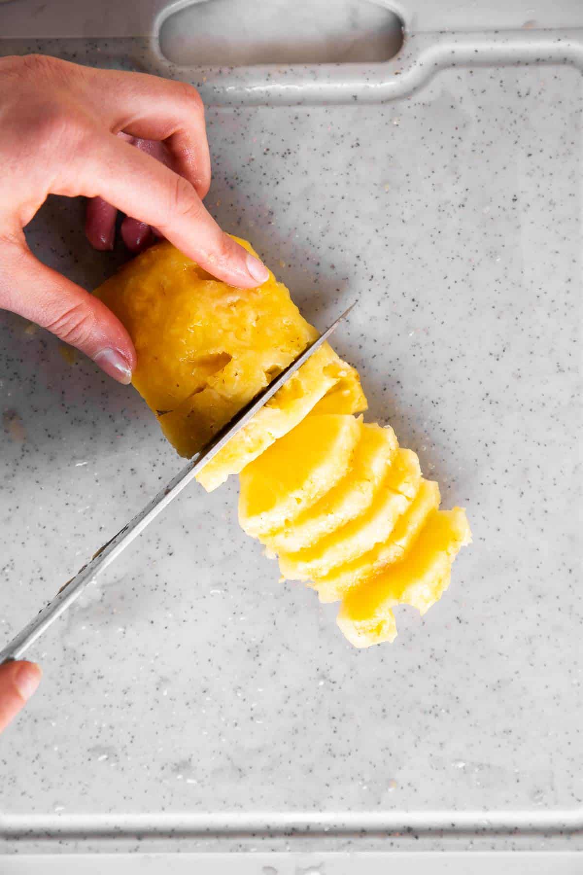 female hand cutting pineapple slices