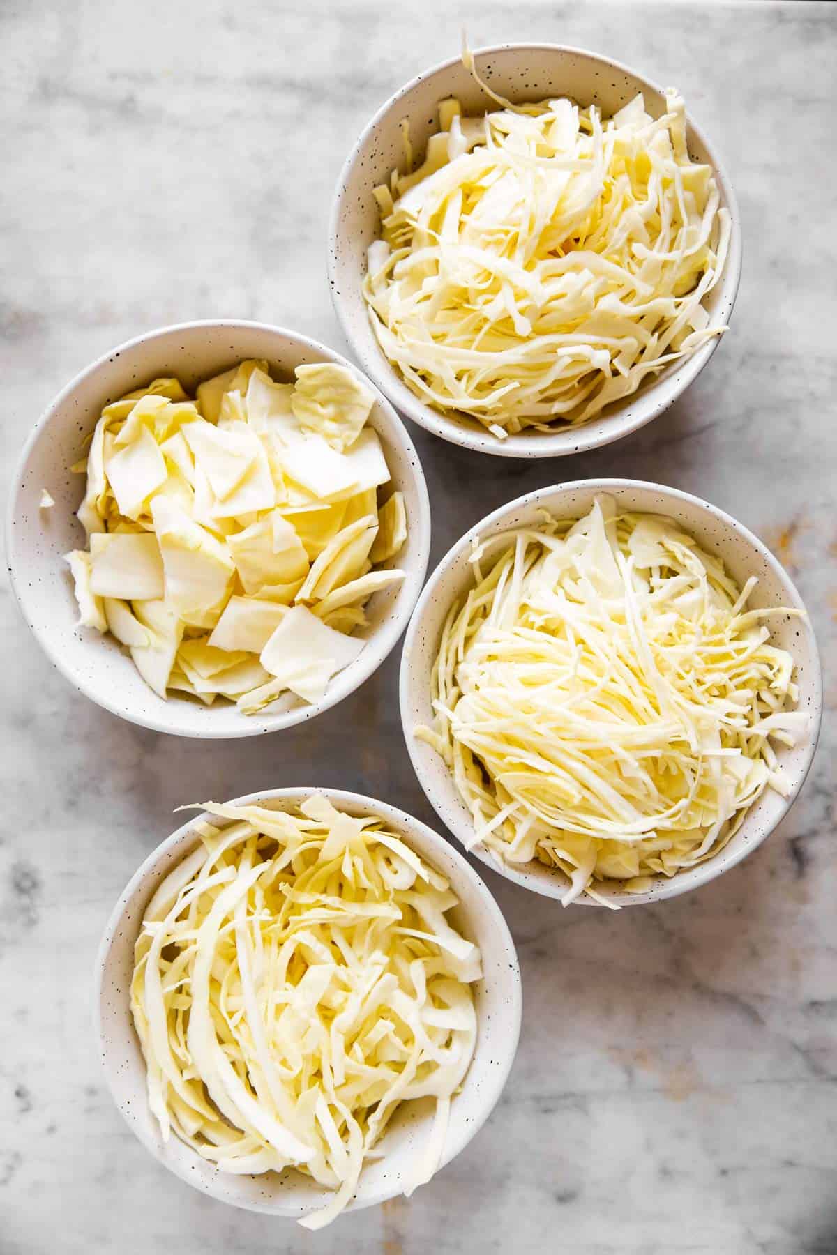 four white bowls with differently sliced cabbage inside