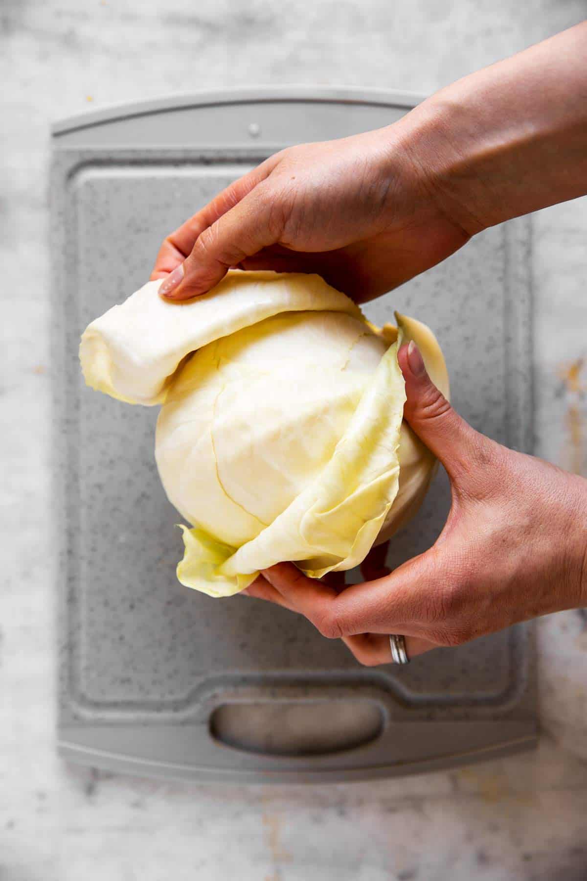female hands removing outer leaves from a white cabbage